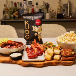 A picture of a bag of Kudo protein popcorn surround with other party favorites. 